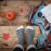 someone's feet in comfy socks is stood on steps with a blanket and a book open beside the feet and pumpkins the other side it looks like they are stood on wooden steps and we are seeing from above