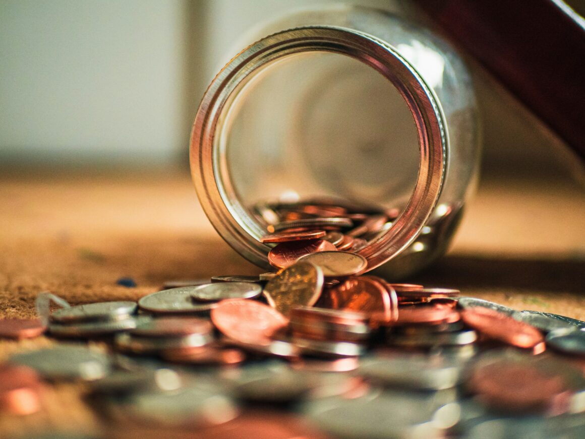 Money in coins are spilling out of a jar on it's side