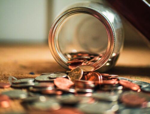 Money in coins are spilling out of a jar on it's side