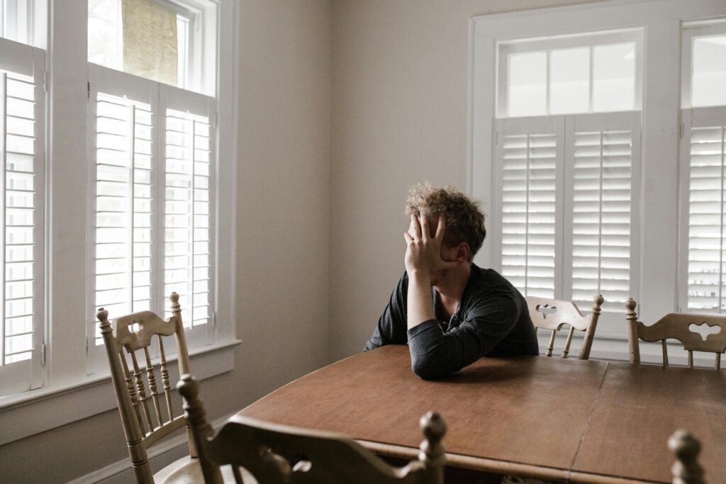 A man is sat at a table, his head is leant on his hand as he looks out of the window