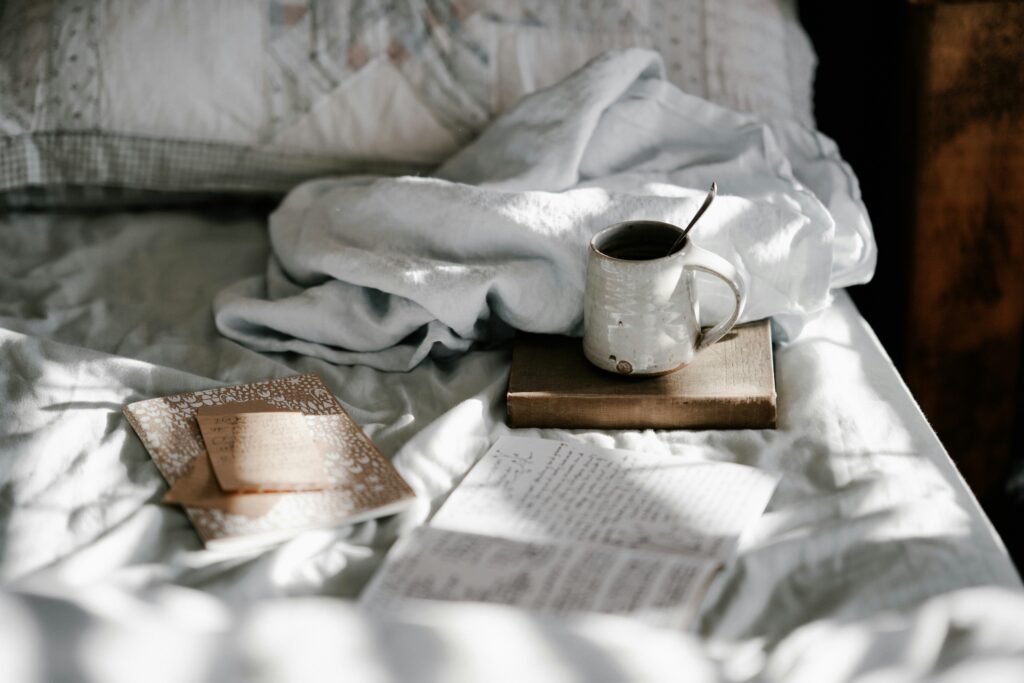 a messy bed with an open book and breakfast spread out on it 