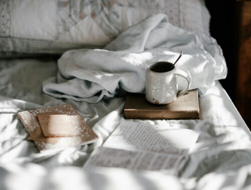 a messy bed with an open book and breakfast spread out on it