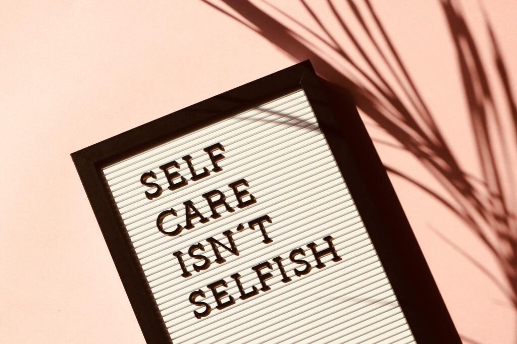 A white board with the words 'self care isn't selfish' written on it in black  against a pink background.