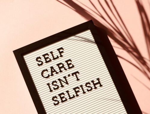 A white board with the words 'self care isn't selfish' written on it in black against a pink background.