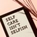 A white board with the words 'self care isn't selfish' written on it in black against a pink background.