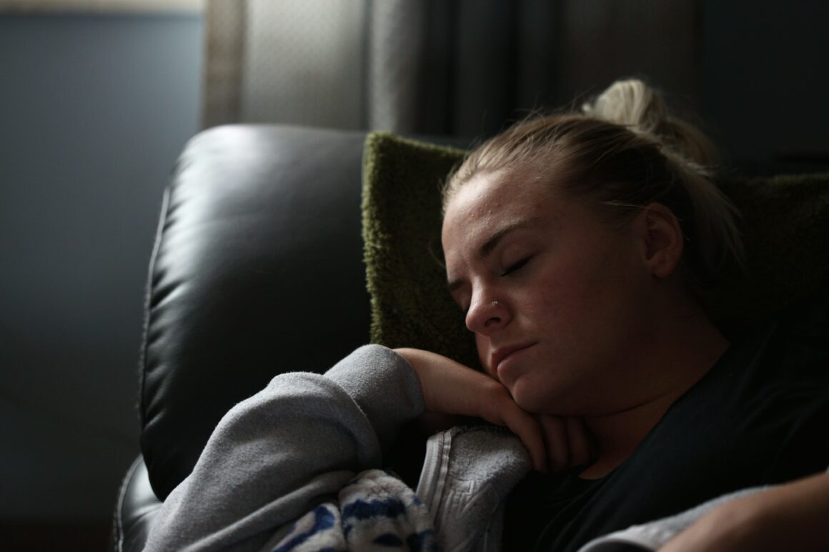 A woman is seen in a dimply lit room, she is curled up on a sofa asleep