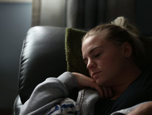 A woman is seen in a dimply lit room, she is curled up on a sofa asleep