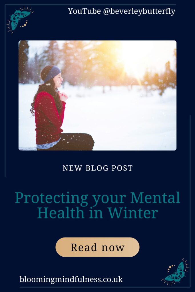 A woman with long hair wearing a red jumper, black trousers and a grey beanie hat is sat in the snow. Behind her is the glow os sunset