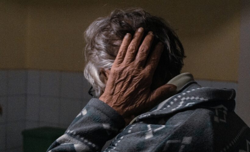 An older woman is seen from the side, her hand is up by her ear obscuring her face.